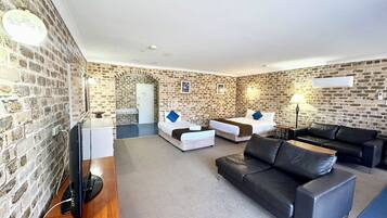 A furnished room with a brick wall, a flat-screen TV, a sofa, a bed, and a small table.