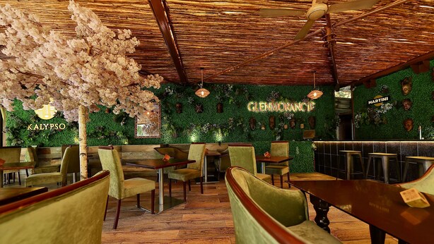 Interior de restaurante con suelo de madera, sillas tapizadas de verde y un ventilador de techo.