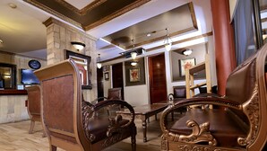 Un vestíbulo amplio con muebles de madera ornamentados, una columna de piedra y un reloj grande en la pared.