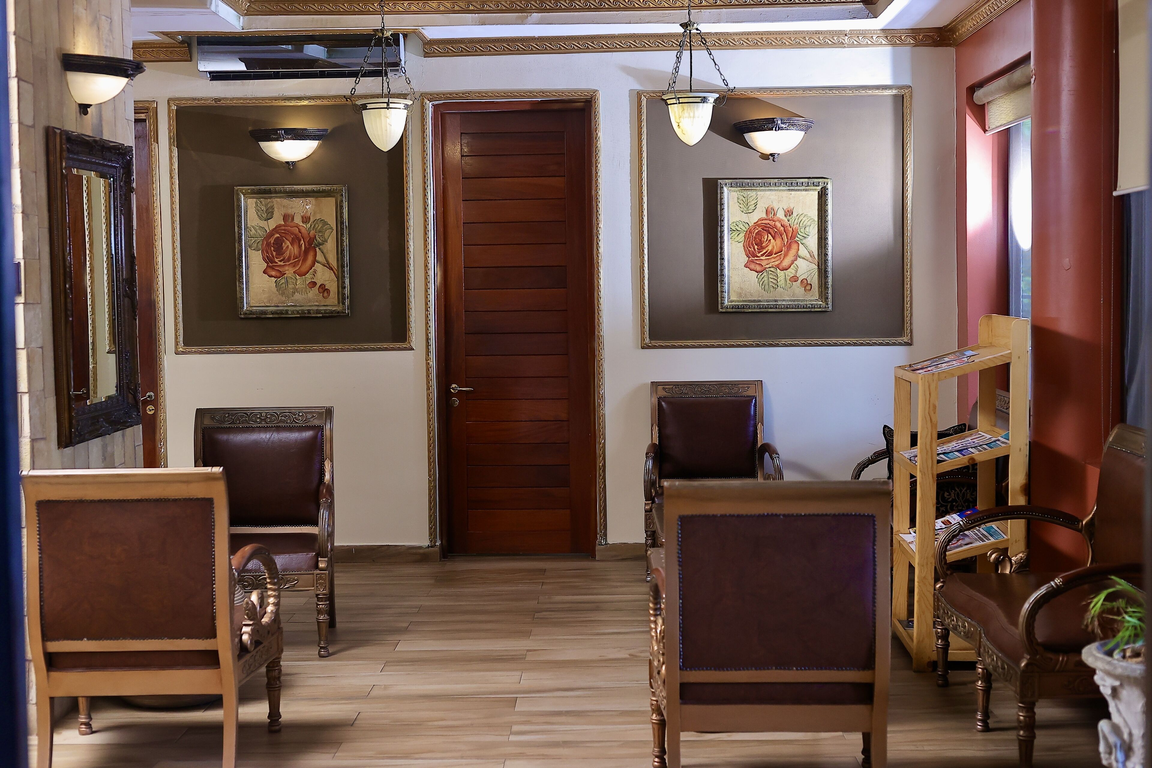 A room with a wooden door, two framed floral paintings, a wooden bookshelf, and two leather chairs.