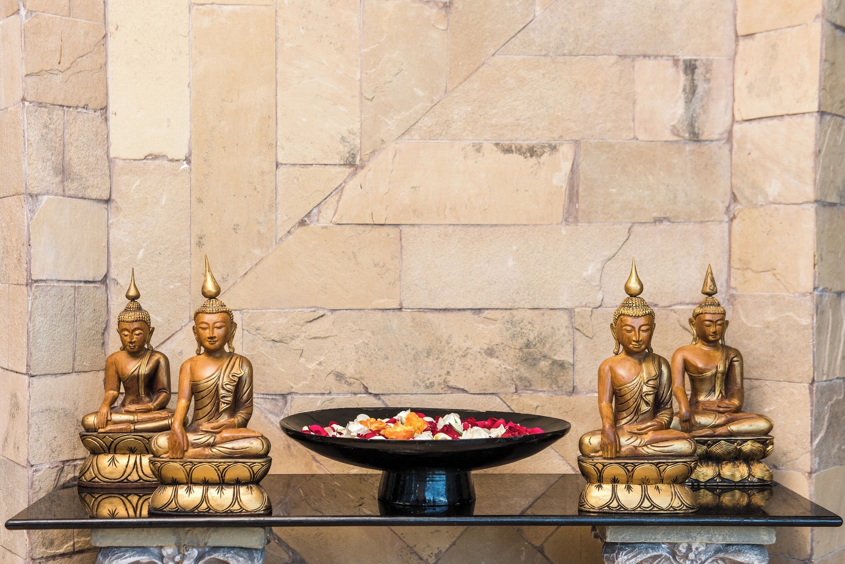 Une table sur laquelle reposent deux statues de Bouddha dorées et un vase rempli de fleurs.