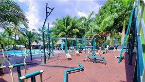 Un área exterior para ejercitarse con varios equipos de gimnasia, bancos y una piscina.
