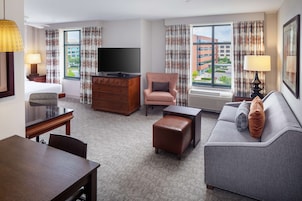 Habitación de hotel con televisión de pantalla plana, sofá, silla, mesa de comedor y cómoda.