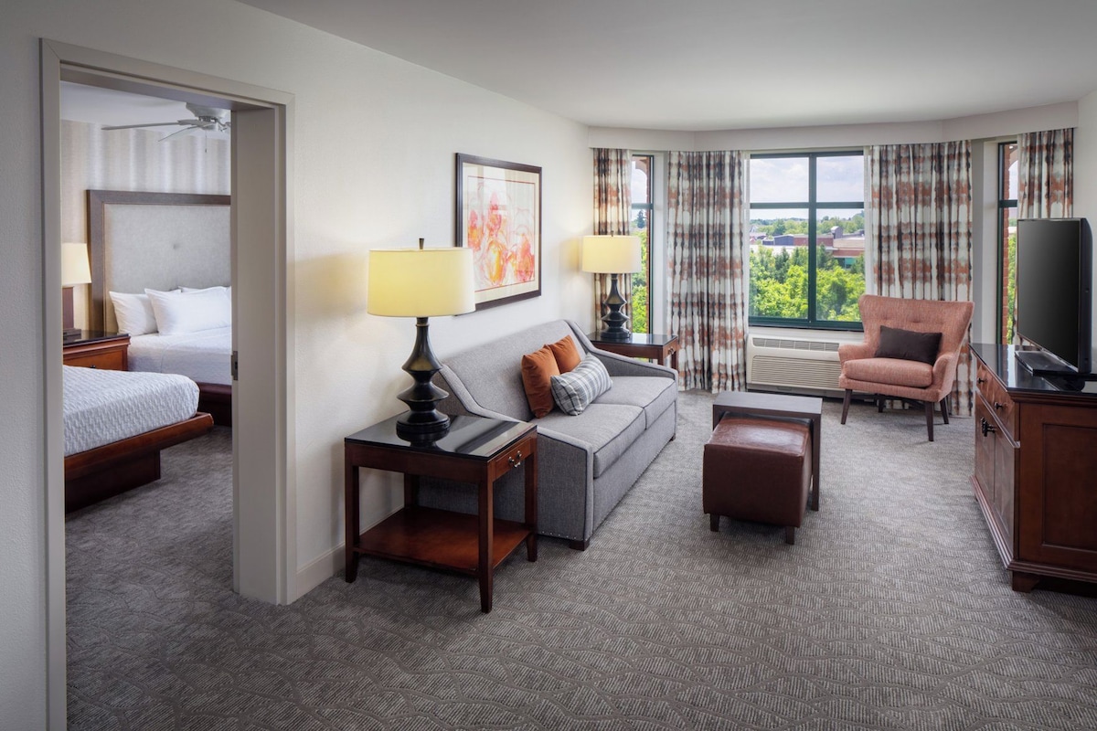 A hotel room with a bed, a sofa, a TV, a desk, and a chair.