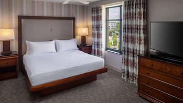 A hotel room with a large bed, two bedside lamps, a TV, a dresser, and a window with curtains.