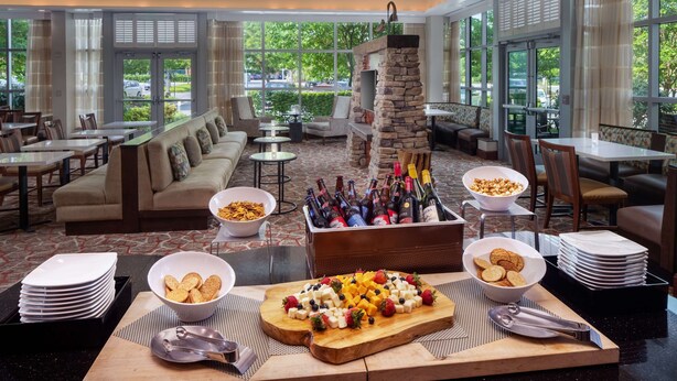 A hotel dining area with a buffet setup, including a variety of food items, a beverage cooler, and seating arrangements. - Homewood Suites by Hilton Rockville-Gaithersburg (Rockville)