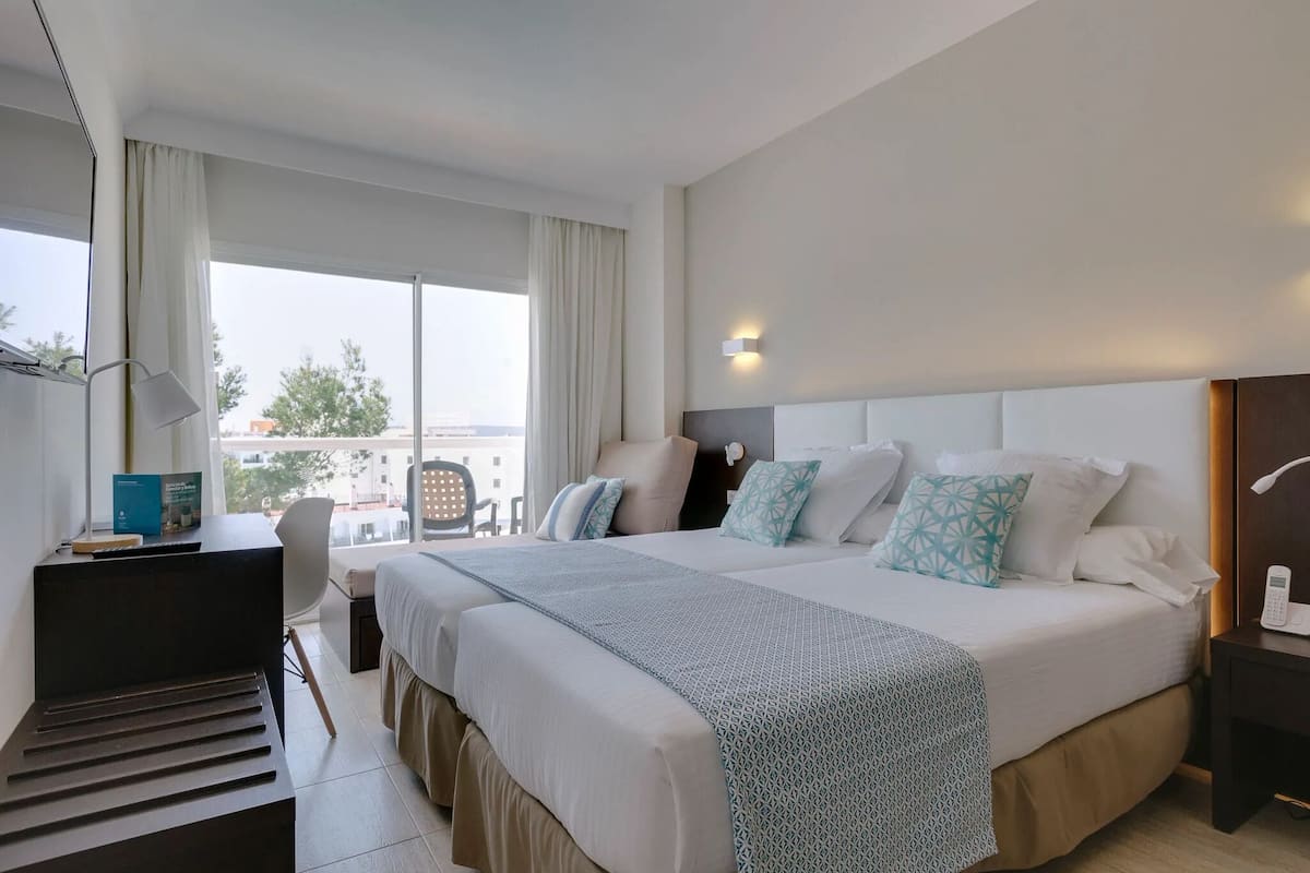 Une chambre d’hôtel avec un grand lit, un bureau, une chaise et une fenêtre avec des rideaux.
