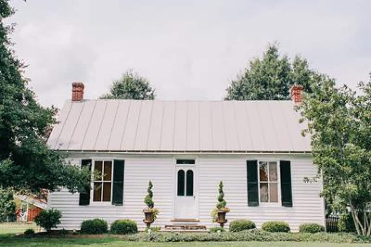 A white building with a gabled roof, a front door, and two windows on the ground floor.