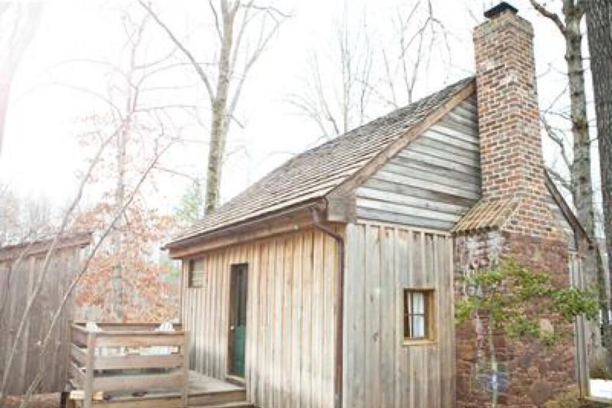 A small wooden cabin with a brick chimney, a wooden porch, and a window.