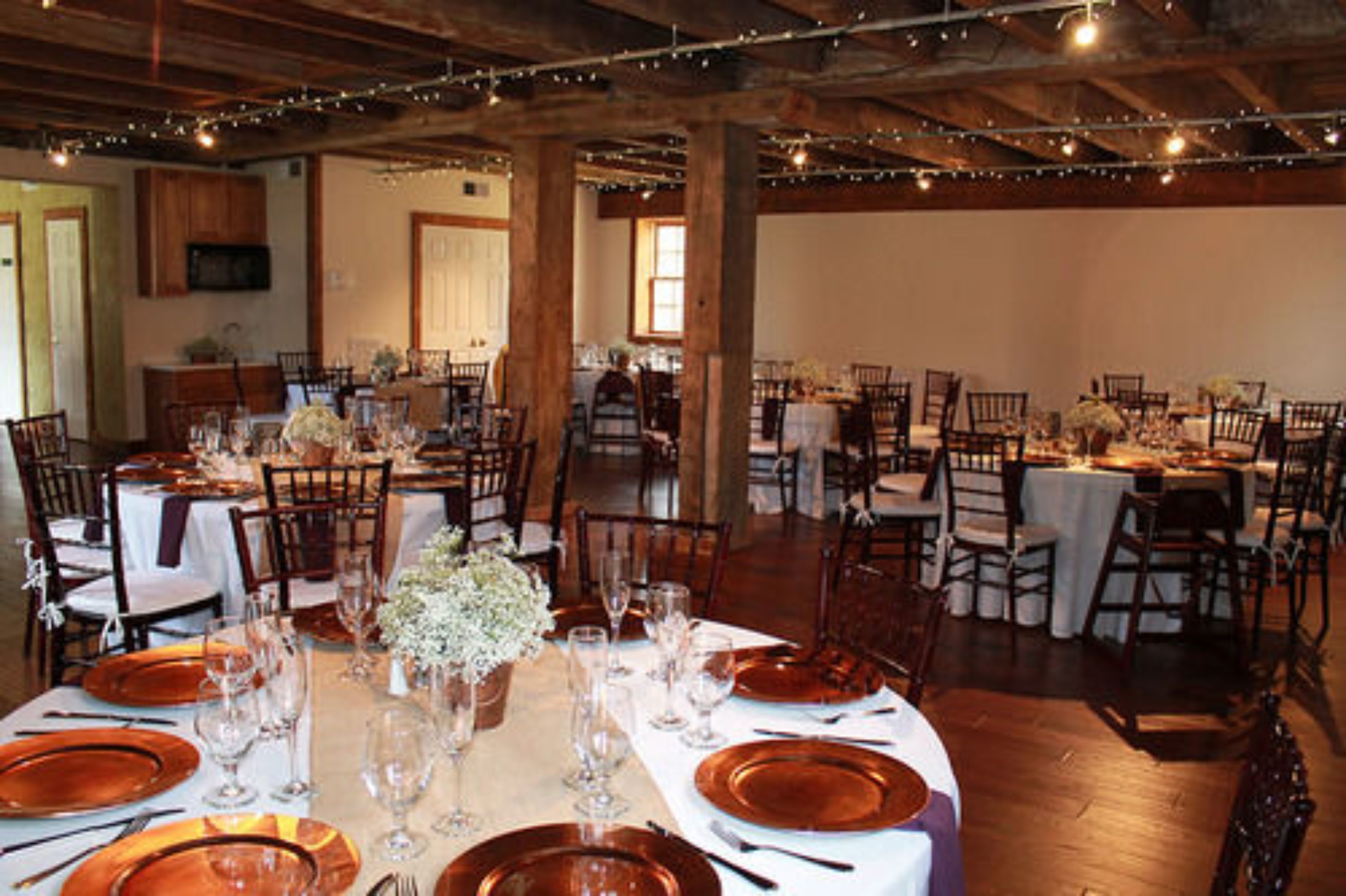 A banquet hall with round tables set for a formal event, featuring white tablecloths and brown plates.