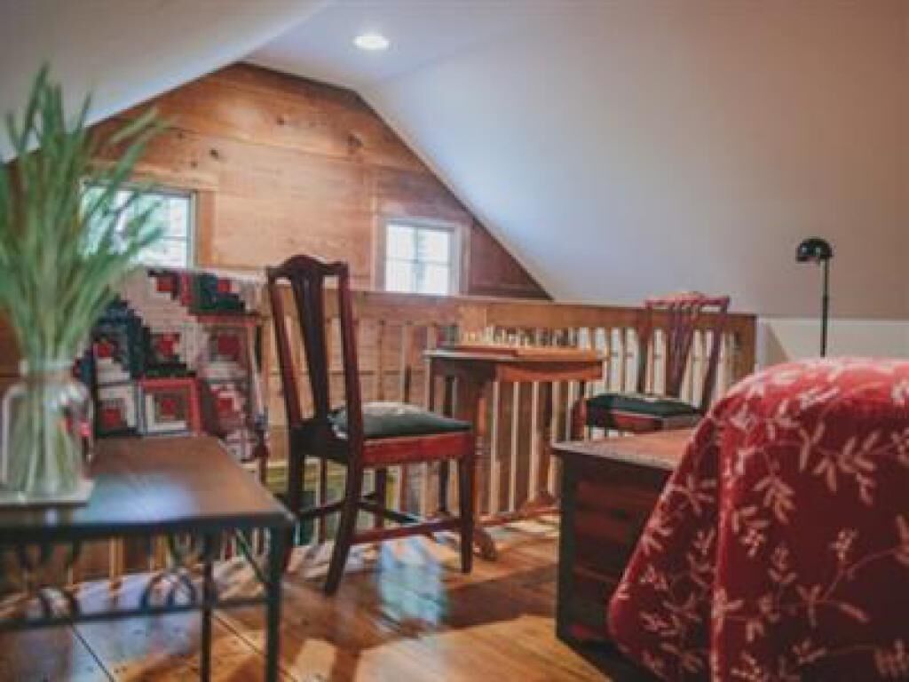 Um quarto de sótão acolhedor com teto inclinado, uma escrivaninha de madeira, uma cadeira e uma cama com colcha vermelha florida.