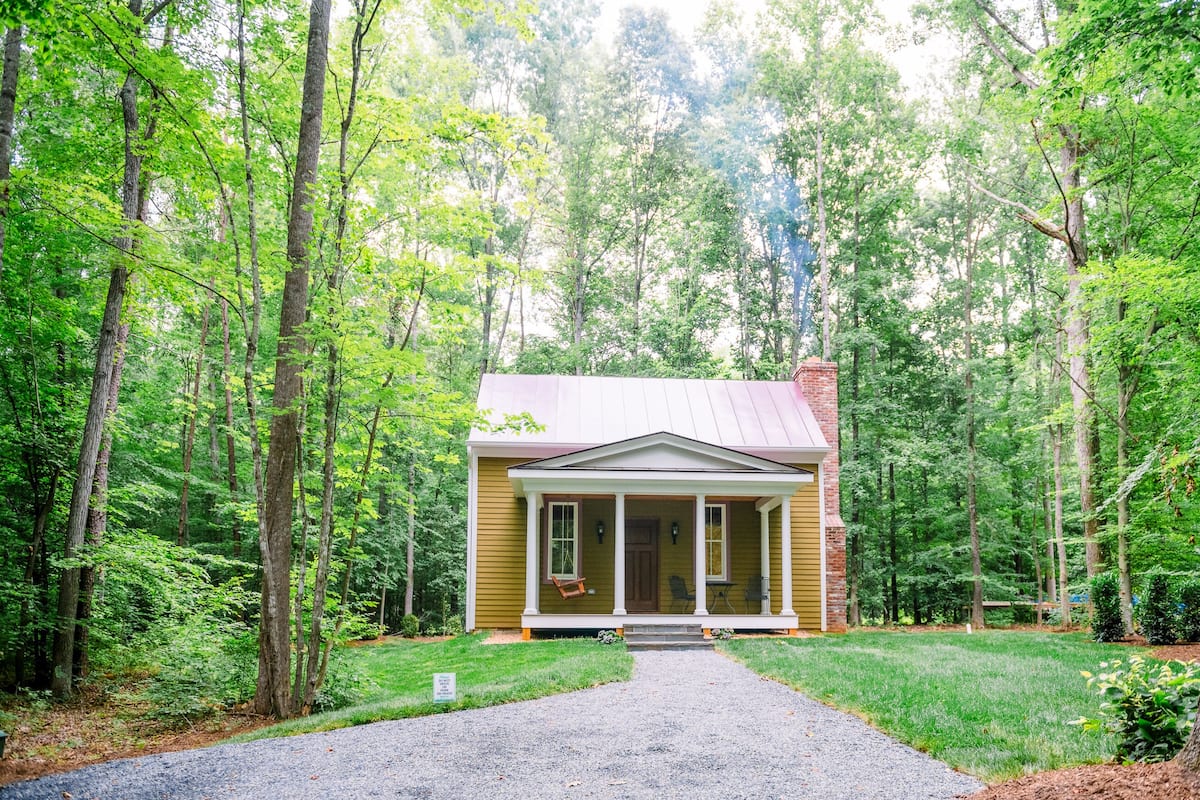 A rustic wooden cabin with a porch, surrounded by dense forest.
