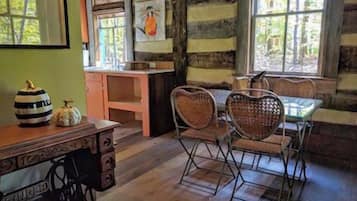 A rustic cabin interior with a wooden dining table, heart-shaped chairs, and a sewing machine.