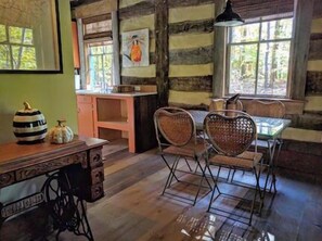 A rustic cabin interior with a wooden dining table, heart-shaped chairs, and a sewing machine.