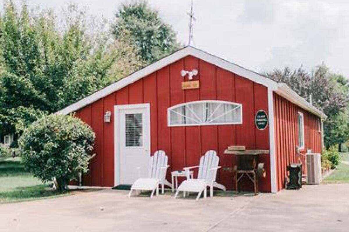 A red building with a white door, two white chairs, and a table outside.