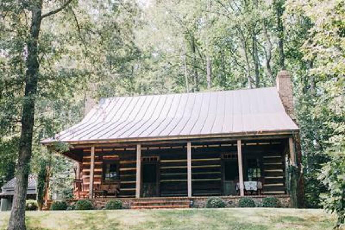 A log cabin with a porch, surrounded by trees.
