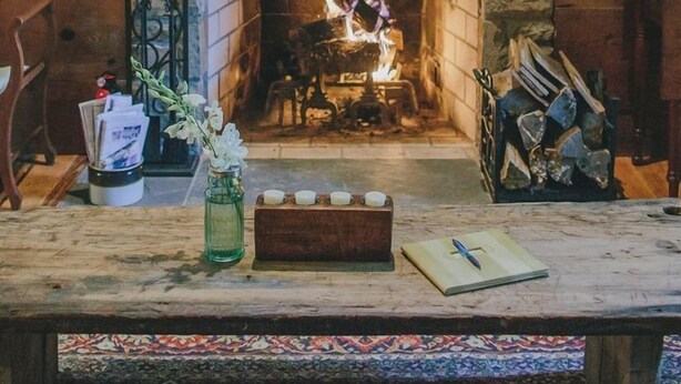 A stone fireplace with a wooden mantel, a window above it, and a table in front with a vase of flowers and candles. - Stevenson Ridge (Spotsylvania)