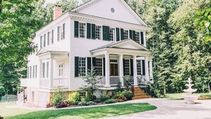 A two-story white house with a front porch, green shutters, and a small garden with a fountain. - Stevenson Ridge (Spotsylvania)