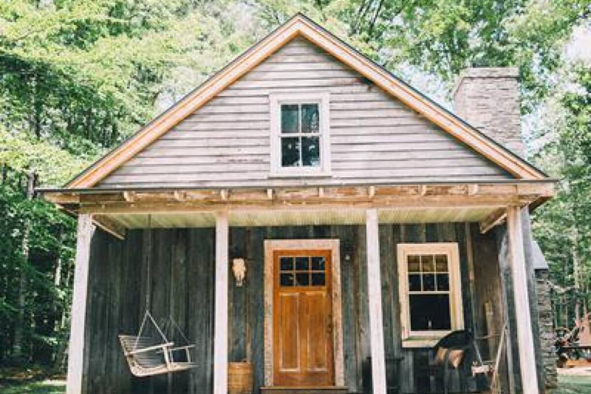 A rustic wooden cabin with a porch, a swing, and a door.