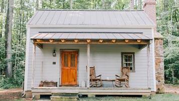 A small, single-story house with a porch, a wooden door, and two rocking chairs.