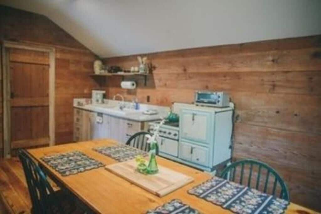 Un interno in legno con un tavolo da pranzo, sedie, angolo cottura con piano cottura e pensili, e soffitto in legno.