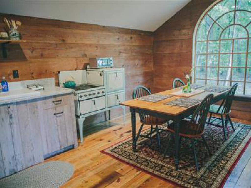 Cocina rústica con paredes y mesa de comedor de madera, además de sillas. Una ventana provee luz natural.