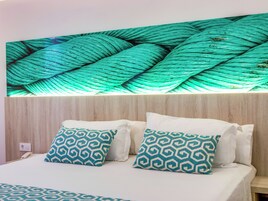 Habitación de hotel con cama, dos almohadas estampadas, una lámpara de pared y un enchufe.