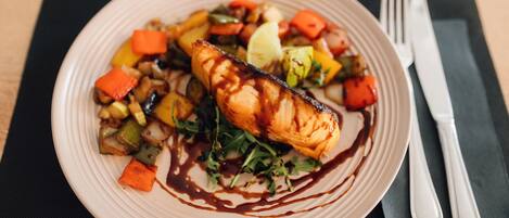 A plate of food with grilled salmon, vegetables, and a drizzle of sauce.