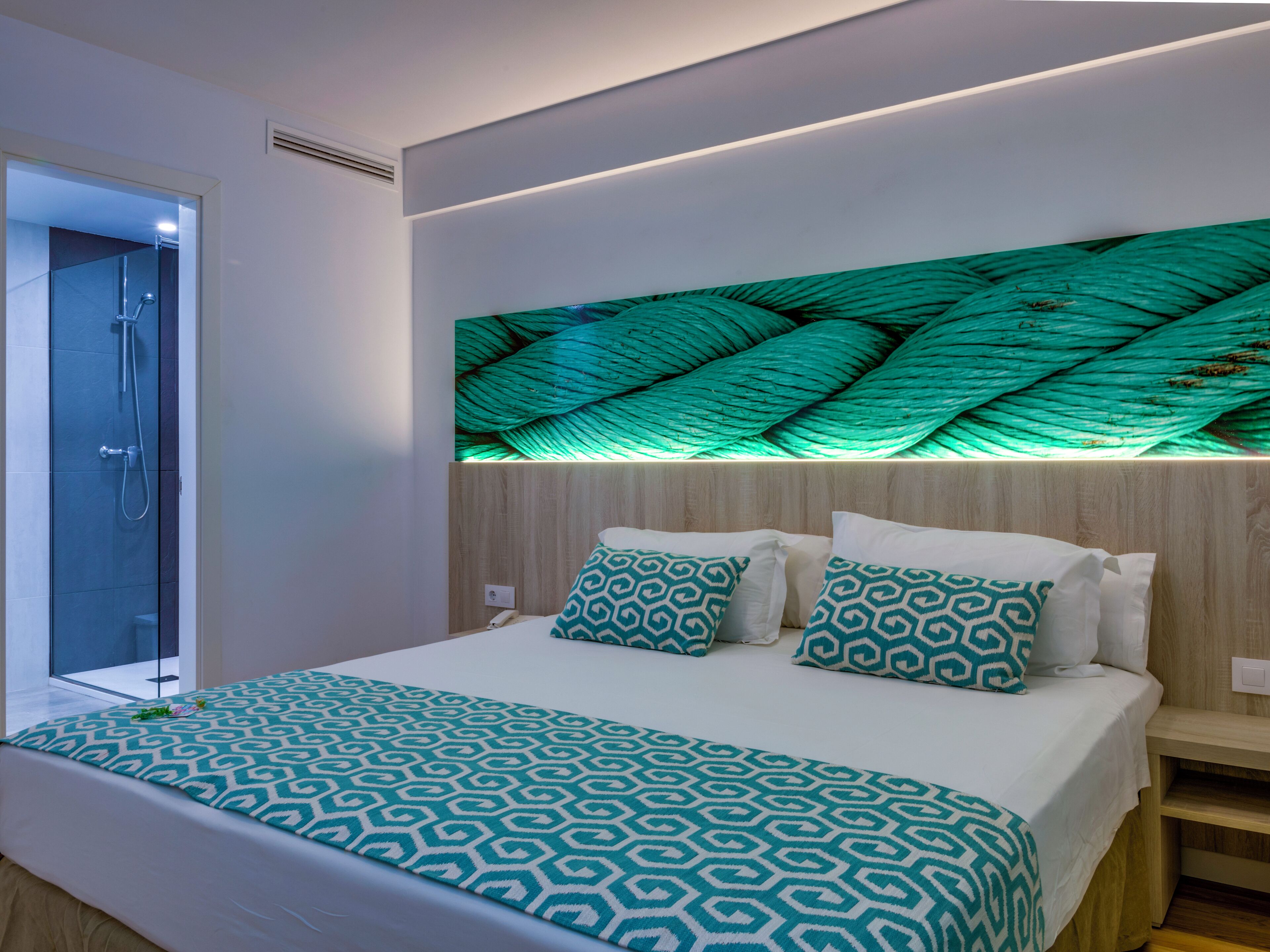 Une chambre moderne avec un lit, une literie à motifs, une tête de lit agrémentée d’une décoration murale texturée et un espace douche.