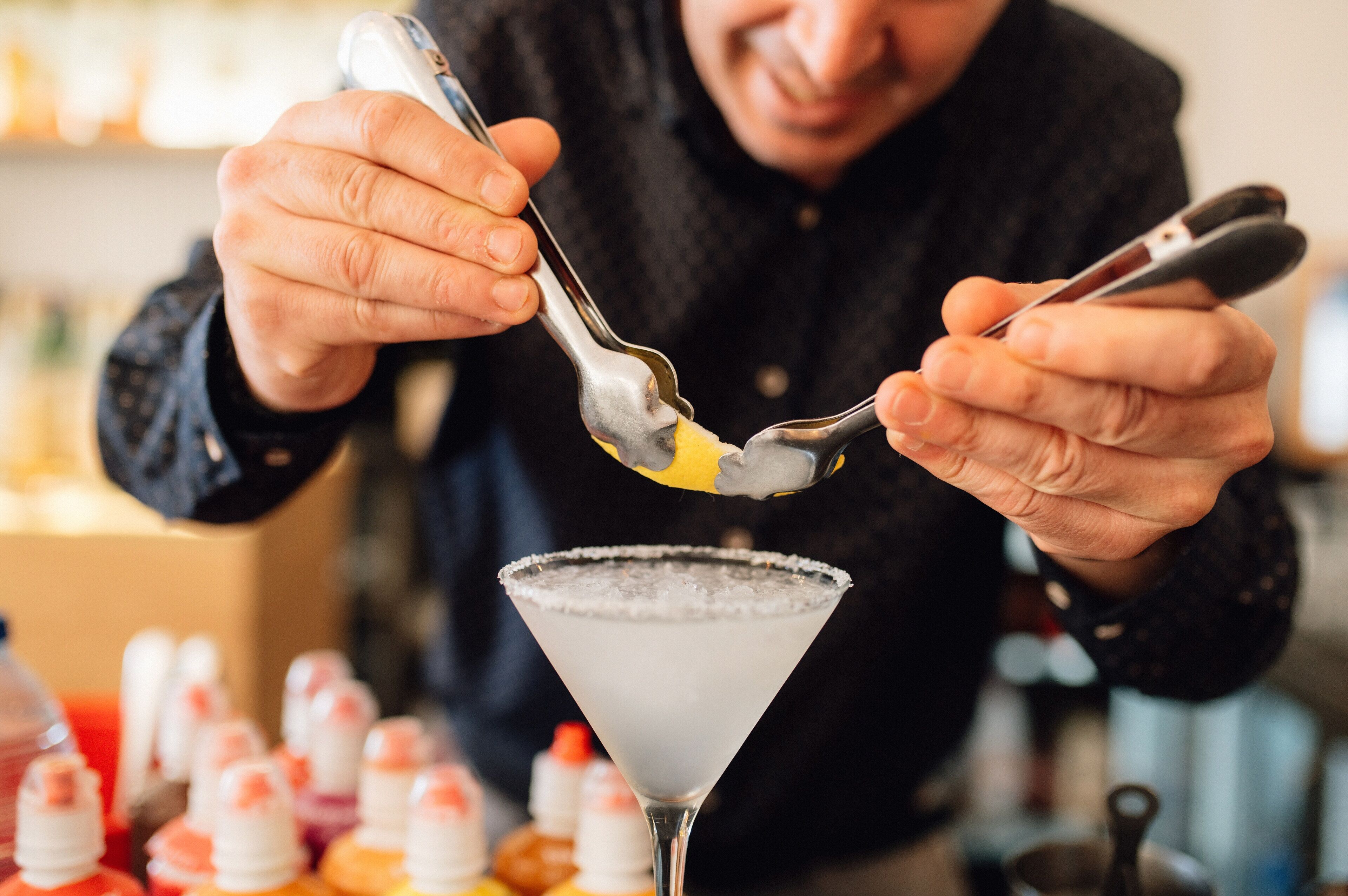 Una persona preparando una bebida con una cuchara y un tenedor, con una copa de martini en primer plano.