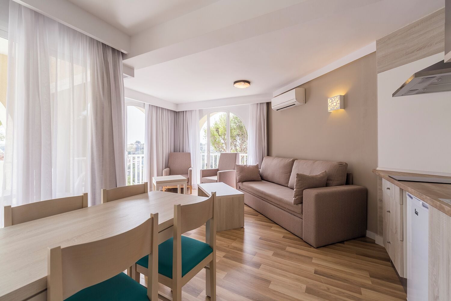 Una sala moderna con una mesa de comedor de madera, un sofá color beige y una cocina con estufa integrada.