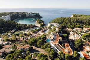 Vista aérea de un resort costero con un puerto deportivo, piscinas y edificios escalonados.