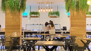 Interior de un restaurante con paneles de madera, plantas colgantes y una barra con la leyenda 'Ensaladas'.