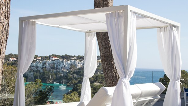 Estructura blanca con toldo y cortinas blancas, con vista a un paisaje costero con acantilados y al mar.