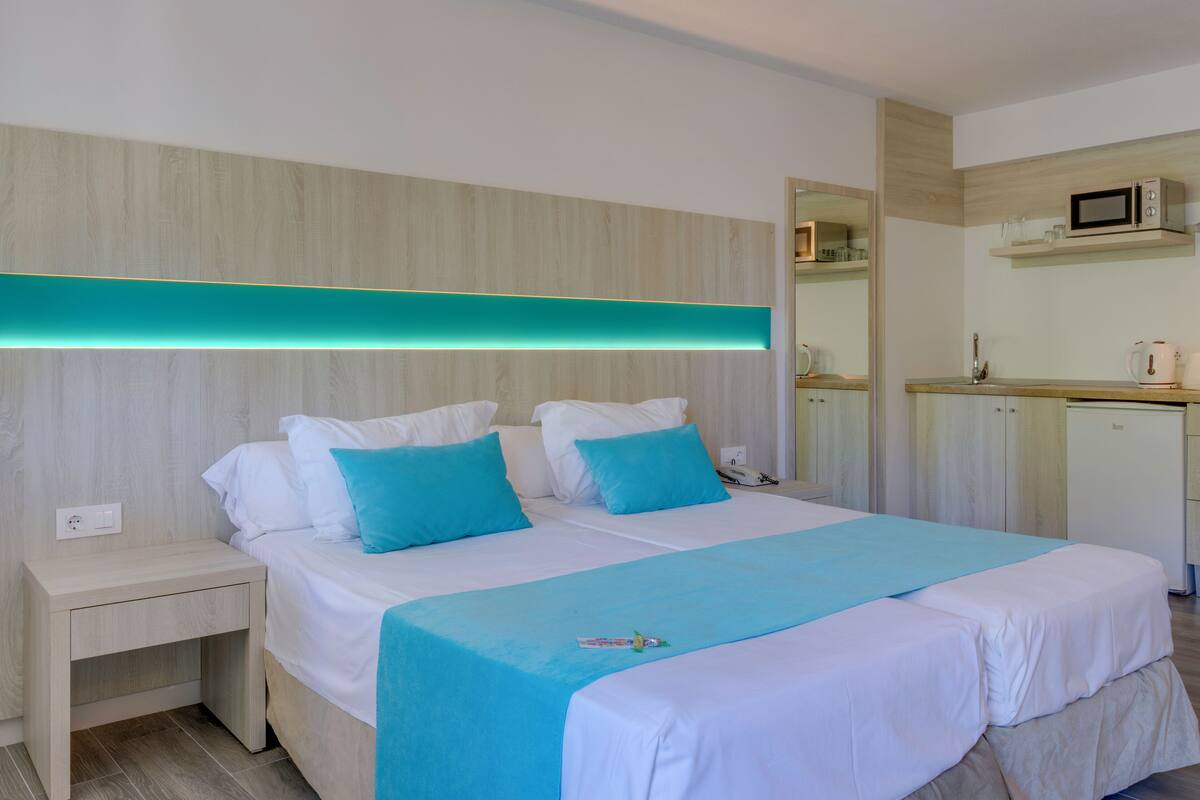 Una habitación de hotel con cama, mesita de noche y una pequeña cocina.