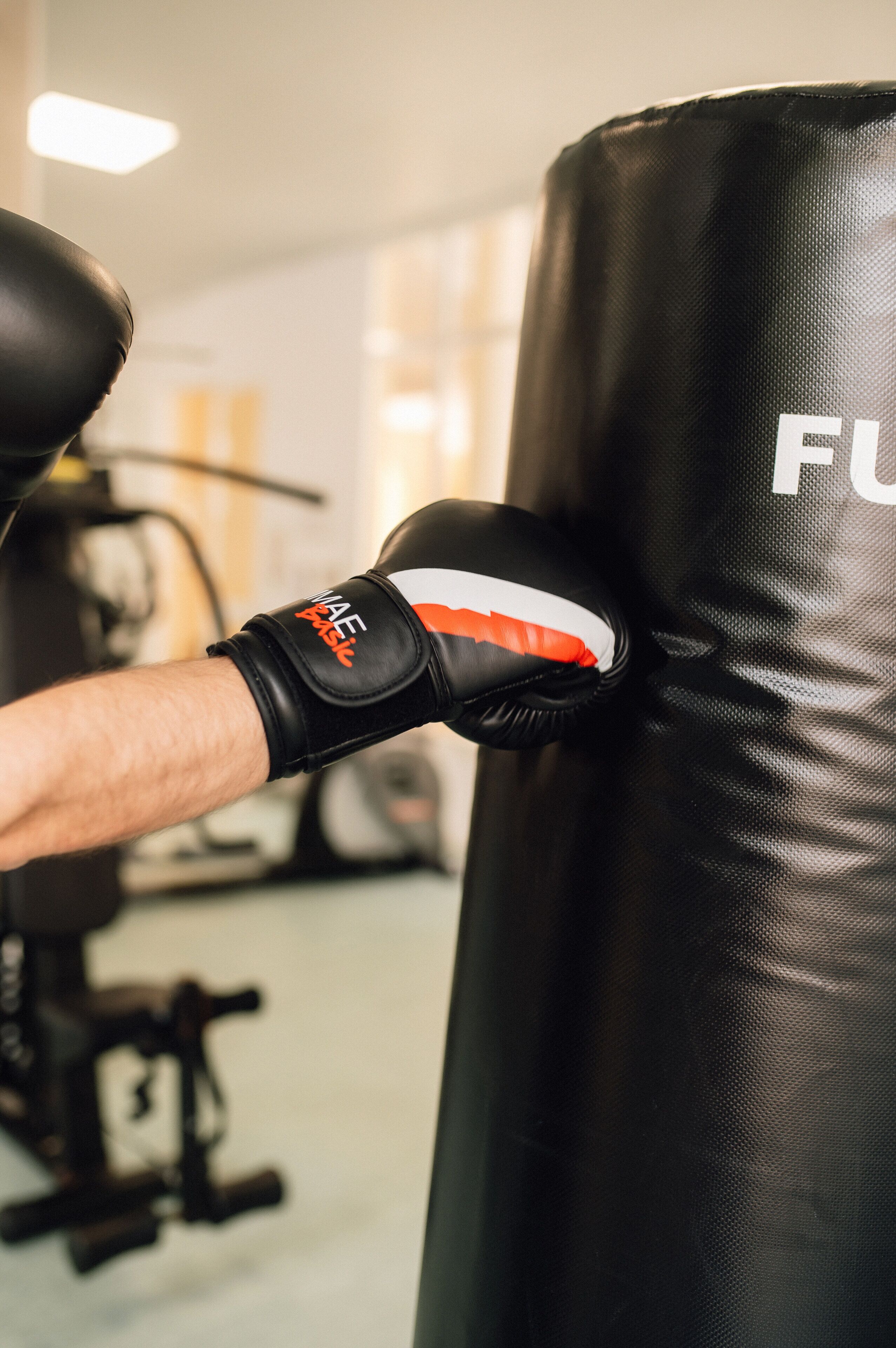 A close-up of a person's arm wearing a black boxing glove with the brand "MAE" visible, positioned against a black punching bag with the letters "FU" partially visible.