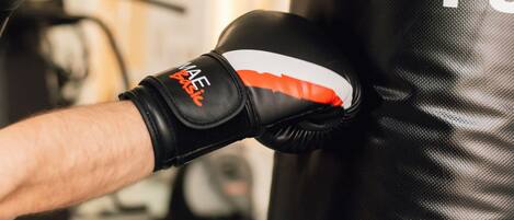 A close-up of a person's arm wearing a black boxing glove with the brand "MAE" visible, positioned against a black punching bag with the letters "FU" partially visible.