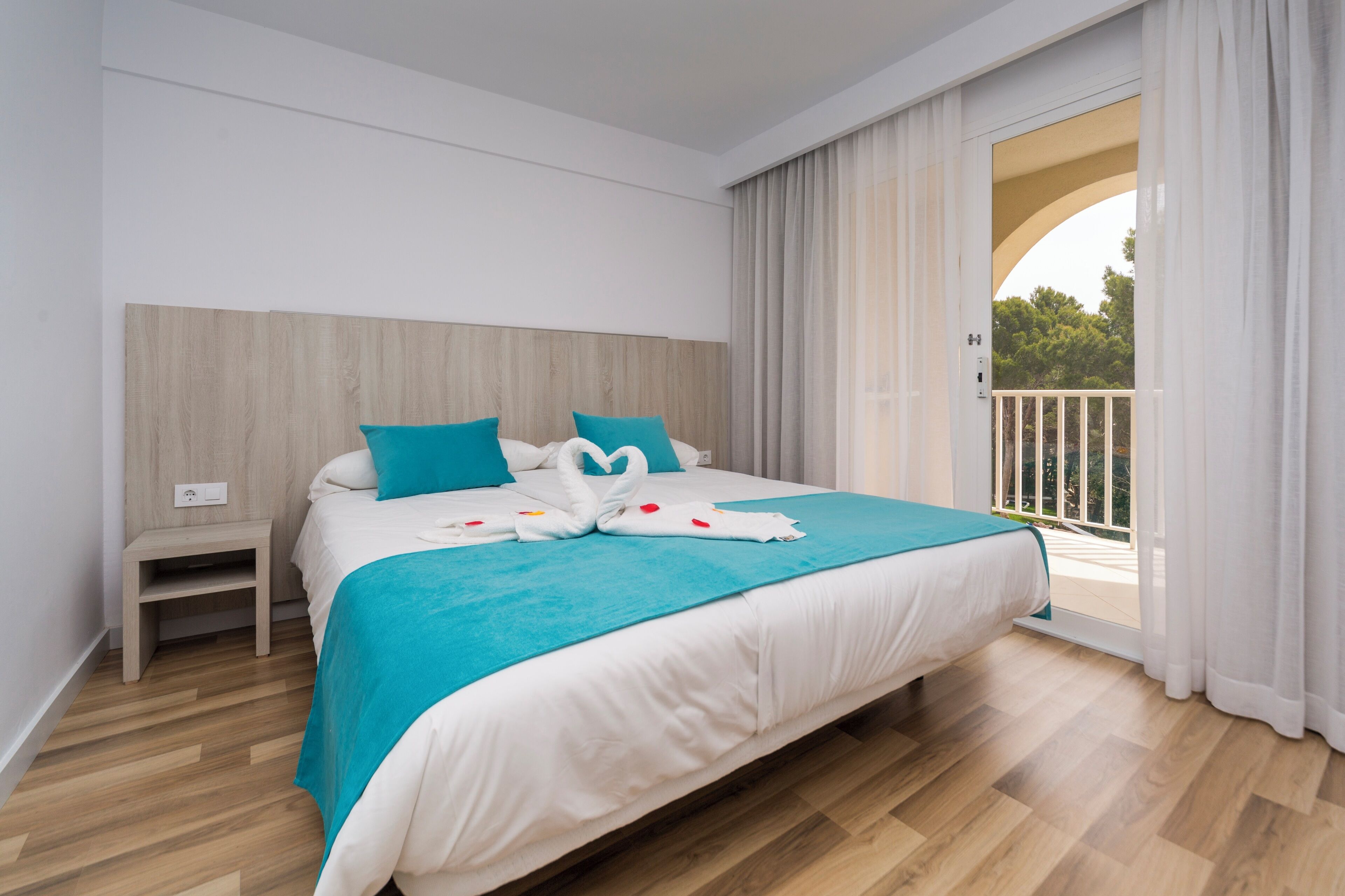 Ein Hotelzimmer mit einem großen Bett, einem Nachttisch und Blick auf einen Balkon.