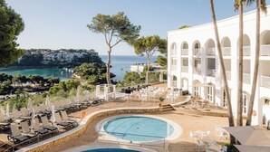 Un resort con piscina, mobiliario exterior y vista al mar.