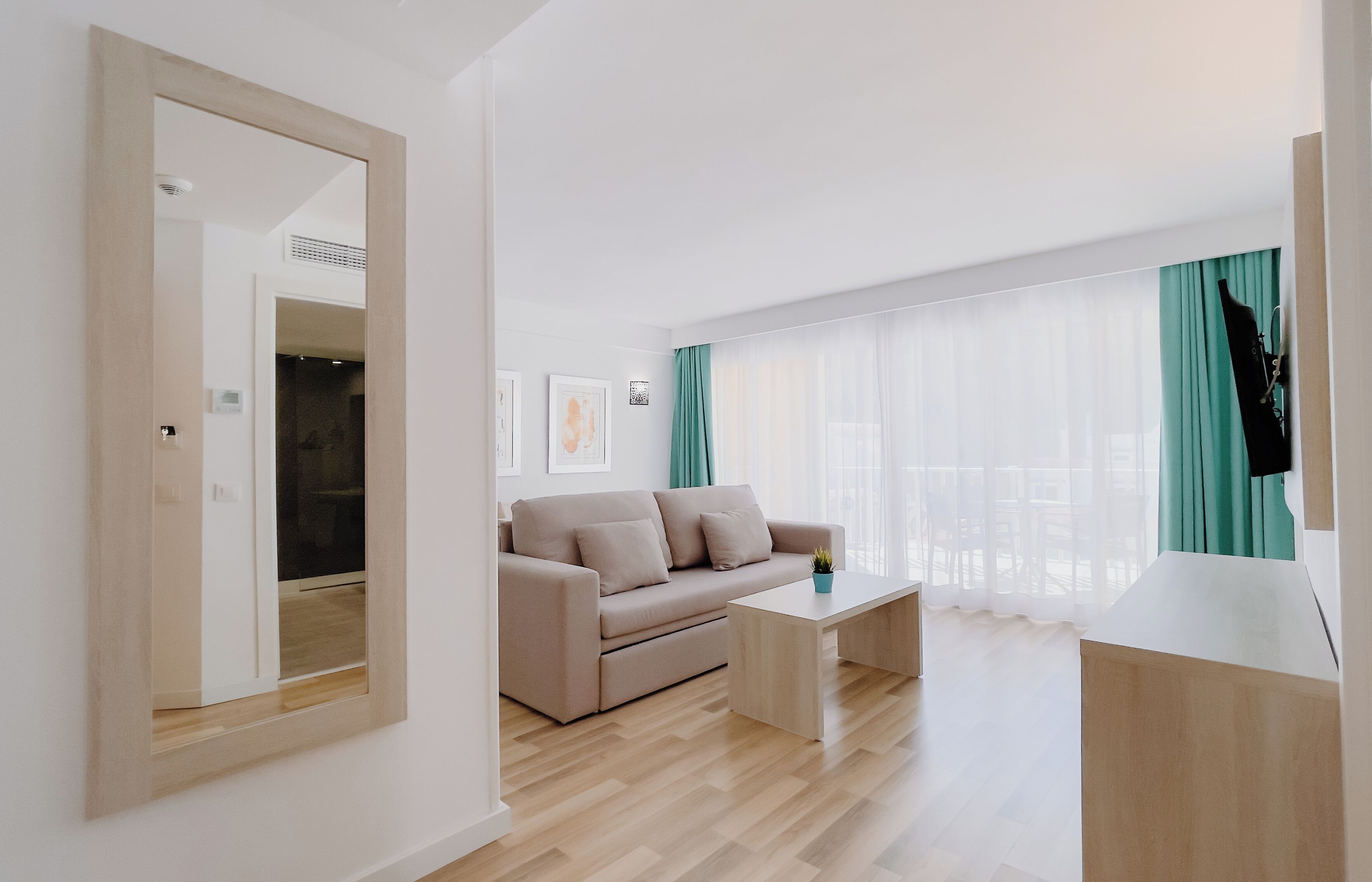 Una sala de estar moderna con un sofá color beige, una mesa de centro de madera y un amplio ventanal con cortinas traslúcidas.