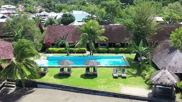 A resort with a swimming pool, lounge chairs, and palm trees.