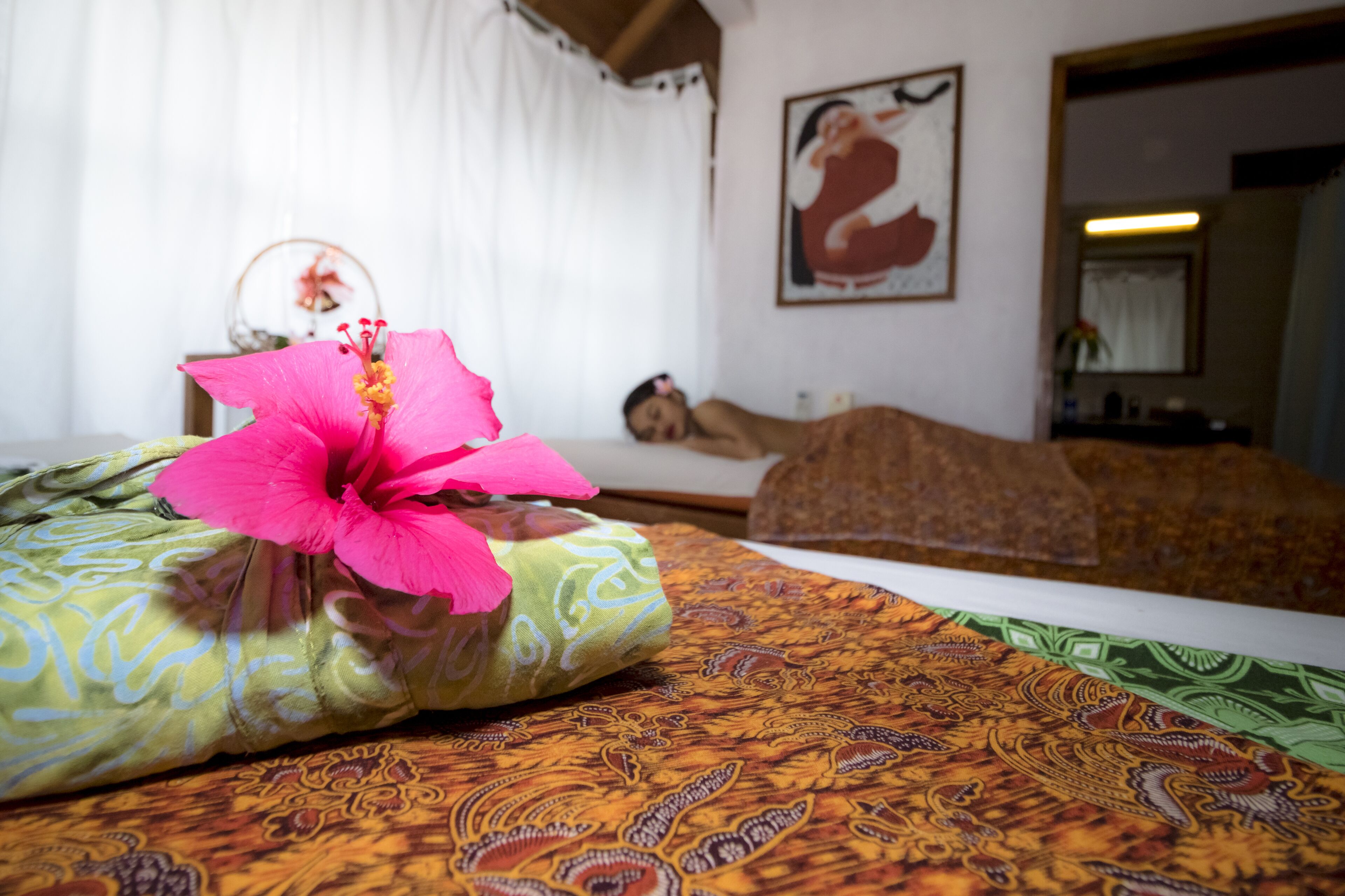 Un lit avec une couvre-lit à motifs, un oreiller orné d’une fleur rose et un tableau accroché au mur.