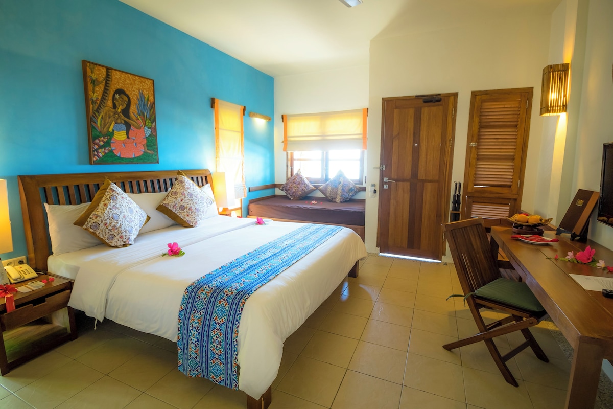 A hotel room with a large bed, a wooden desk, a chair, and a painting on the wall.
