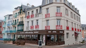 Un edificio de varios pisos con un bar y hotel en la planta baja, con balcones de barandillas rojas y un estilo arquitectónico clásico.