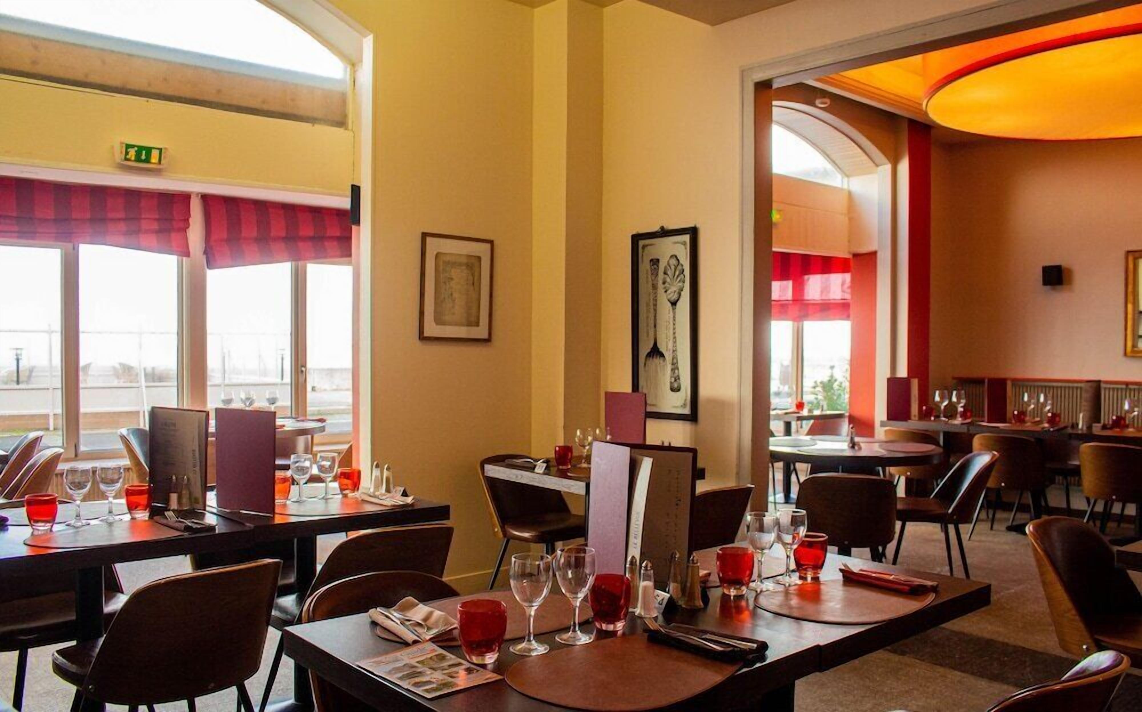 A restaurant with tables set for dining, framed artwork on the walls, and a view through the windows.