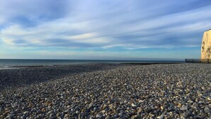 Una playa de arena fina con un acantilado rocoso y una cerca de madera.