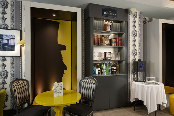 A room with a yellow table and chairs, a bookshelf with books and bottles, and a framed picture on the wall. - Les Plumes Hôtel Paris (Paris)
