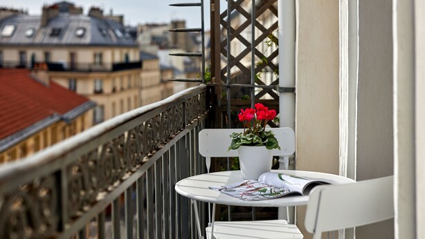 Een balkon met een witte stoel, een tafeltje en een bloempot met rode bloemen.