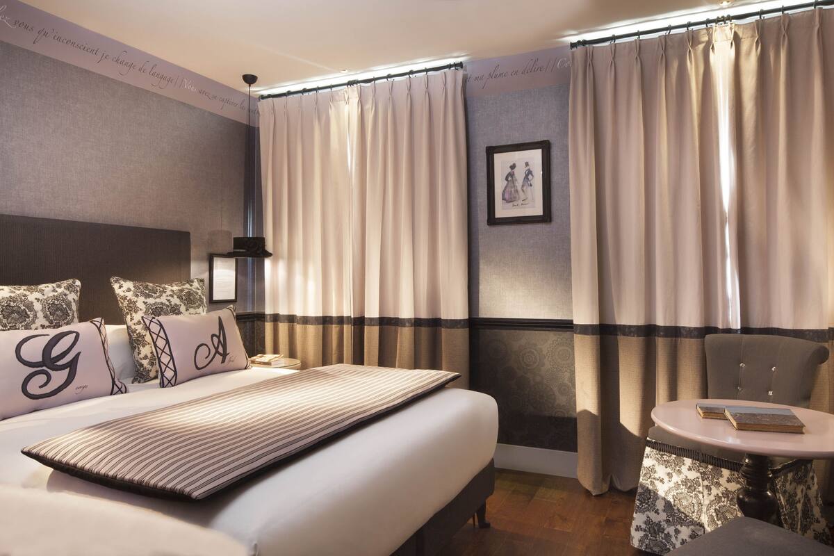 Una habitación de hotel con una cama, una silla, una mesita y cortinas.