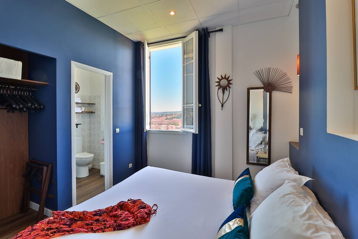 A hotel room with a large bed, a wardrobe, a bathroom, and a view of the city.